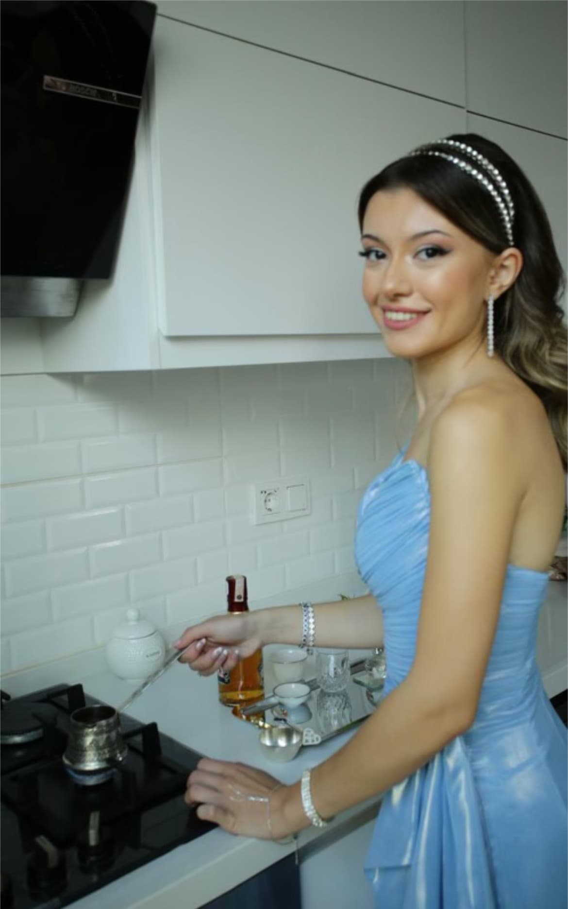 Mavi bir elbise giyen genç kadın, modern bir mutfakta Türk kahvesi hazırlıyor.
